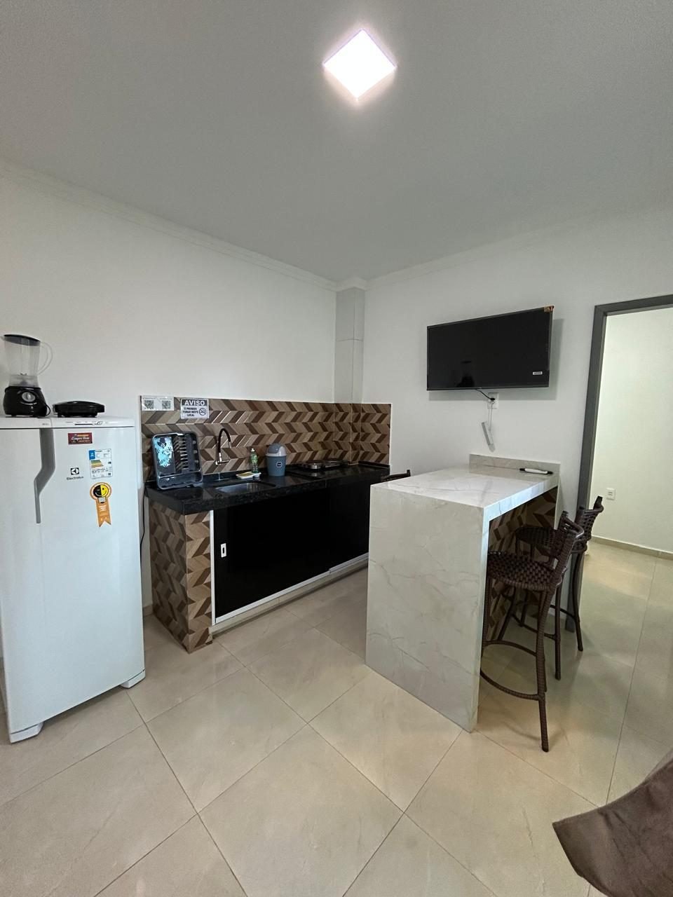Ambiente do flat com cozinha, bancada e TV